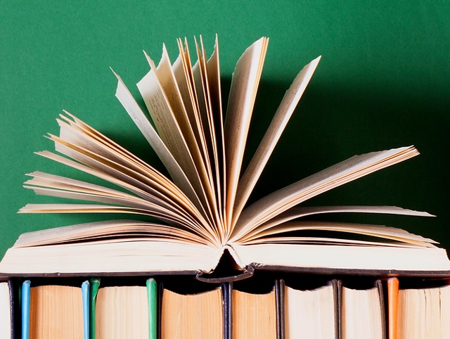 An open book stacked on closed books against a green background.